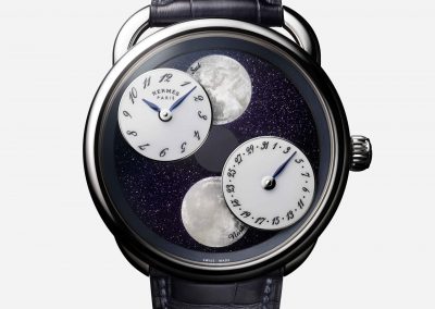 Die Mondscheiben und die rotierenden Uhrzeit-, bzw. Datumsscheibe vor nachtdunkler Oberfläche der hermes Armbanduhr